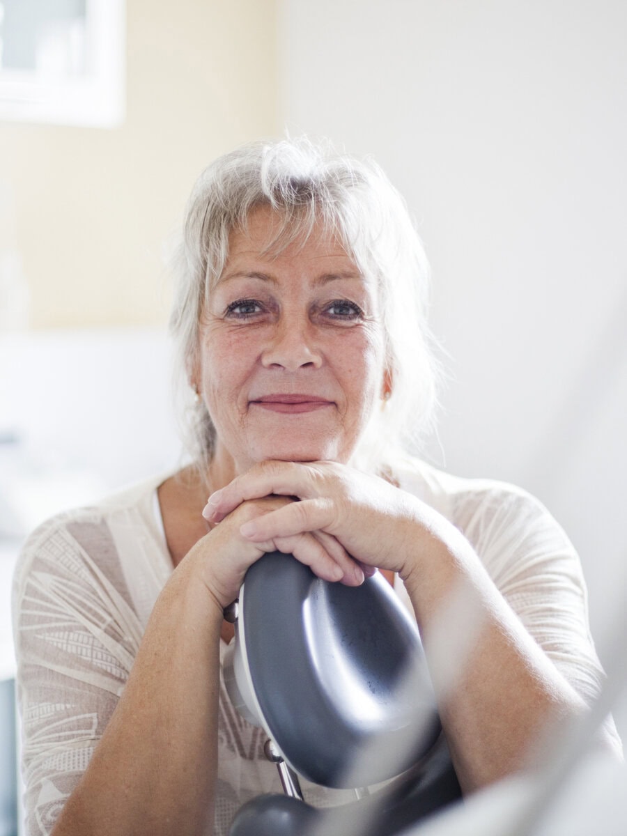 Tandlæge og klinikejer Bente Canter læner sig over en tandlægestol og smiler på sin klinik i Odder